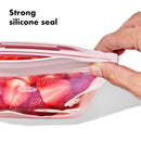 Silicone reusable bag with strawberries inside, showcasing a strong silicone seal and a hand securing the lid.