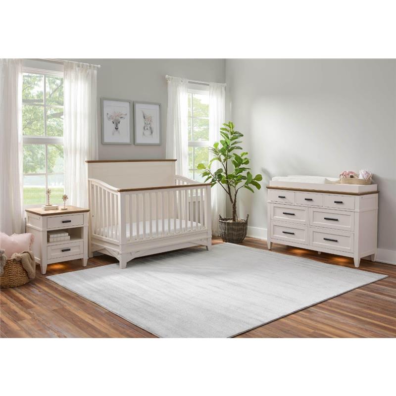 Artisian 7-drawer dresser with lights in a nursery setting, featuring a crib, nightstand, and potted plant.