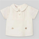 Cream short-sleeve newborn shirt features a pleated front, button closure, and rounded collar, designed for baby boys.