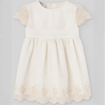 Cream sleeveless baby dress with lace cap sleeves and embroidered floral details along the hem.