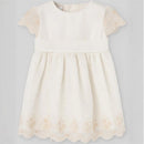 Cream sleeveless baby dress with lace cap sleeves and embroidered floral details along the hem.
