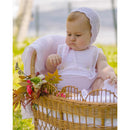 Baby dressed in pastel pink garment sitting in a woven basket decorated with flowers, surrounded by greenery.
