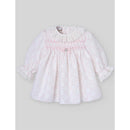 Light pink woven newborn dress with long sleeves, smocked bodice, lace collar, and a decorative button at the center.