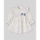 Woven newborn dress in cream with floral print, ruffled neckline, and blue bow detail. Perfect for infants.