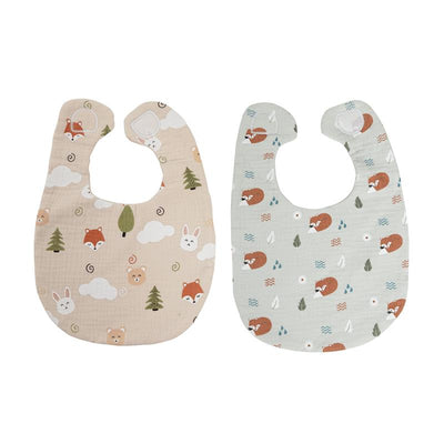 Two muslin cotton baby bibs featuring woodland animals: one tan with foxes and trees, the other light gray with sleeping foxes and raindrops.