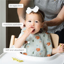 A baby in a high chair wearing a soft, absorbent muslin cotton bib featuring woodland animal patterns, with text highlighting its machine washable feature.