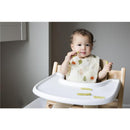 Baby seated in a high chair wearing a woodland-themed muslin cotton bib, enjoying snacks on a tray.