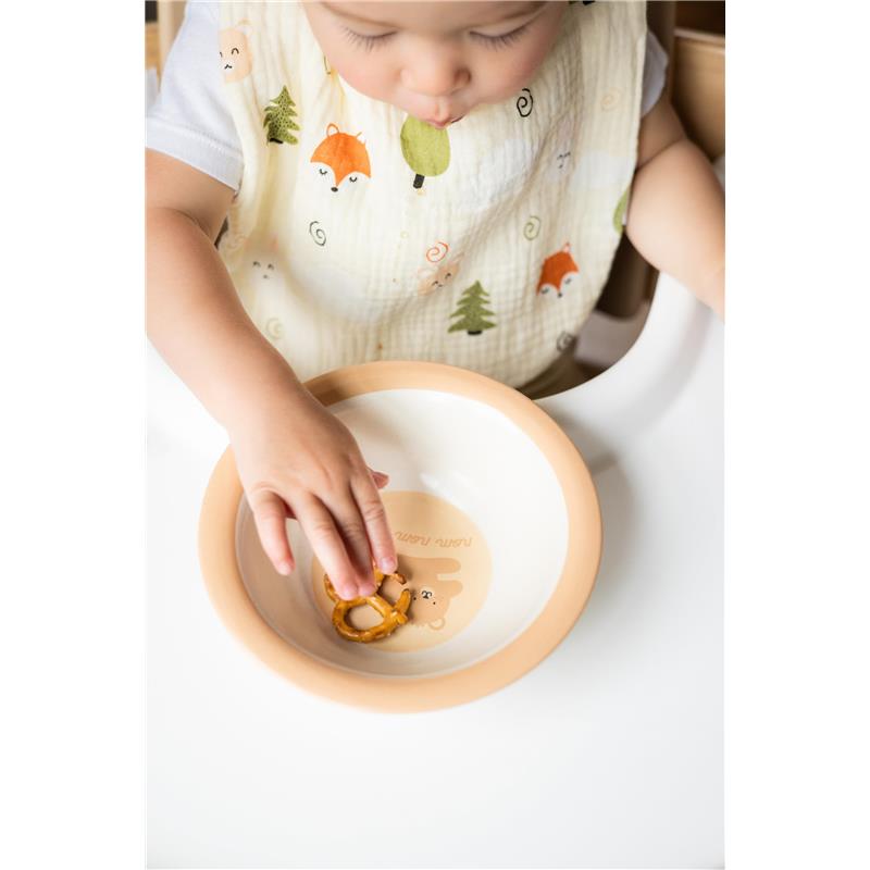 Toddler wearing a muslin cotton bib with woodland animals, reaching for a pretzel in a bowl.