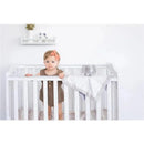 Toddler in a crib with a gray elephant security blanket lovey, wearing a brown outfit and orange headband.