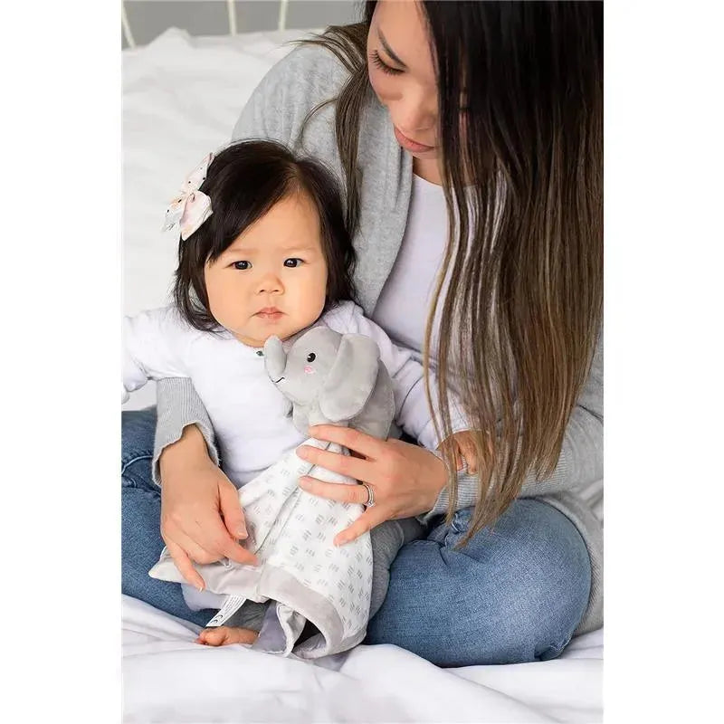 Young child holding a gray elephant security blanket lovey, cuddled in the lap of a woman in a cozy setting.