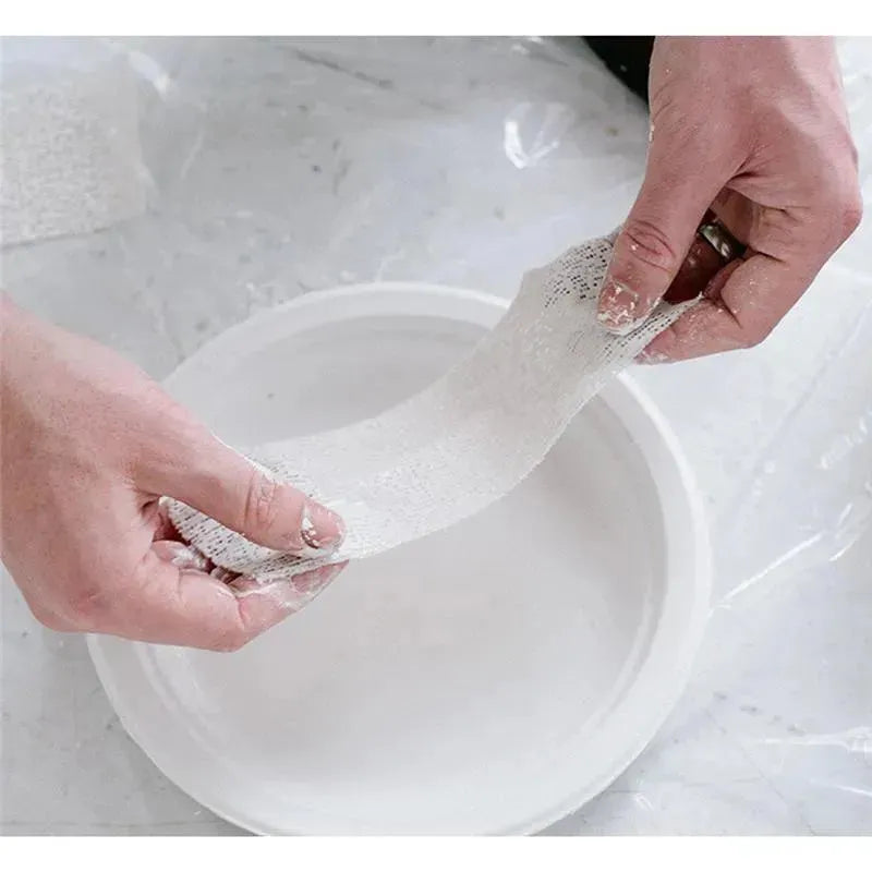 Hands holding a strip of casting material above a white bowl, preparing for a belly cast with the Pearhead Belly Casting Kit.