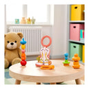 Colorful Pearhead cowboy boot teether ring on a wooden table, surrounded by stacking rings and pacifiers in a bright room.