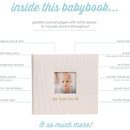 Ivory linen baby memory book with a framed photo window, featuring guided journal pages for capturing milestones and memories.