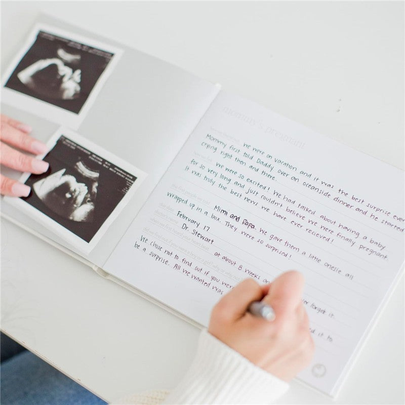 Ivory linen baby memory book open to ultrasound photos and handwritten notes about the pregnancy journey.