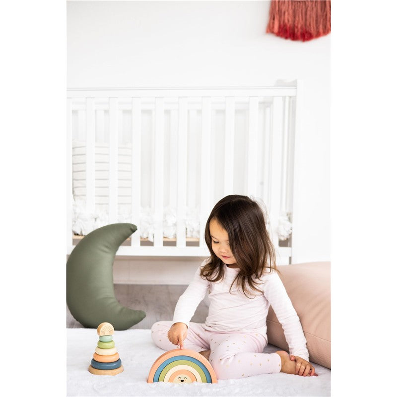 Child sitting on a soft surface, playing with the Pearhead Wooden Rainbow Stacking Toy, featuring pastel-colored arches.