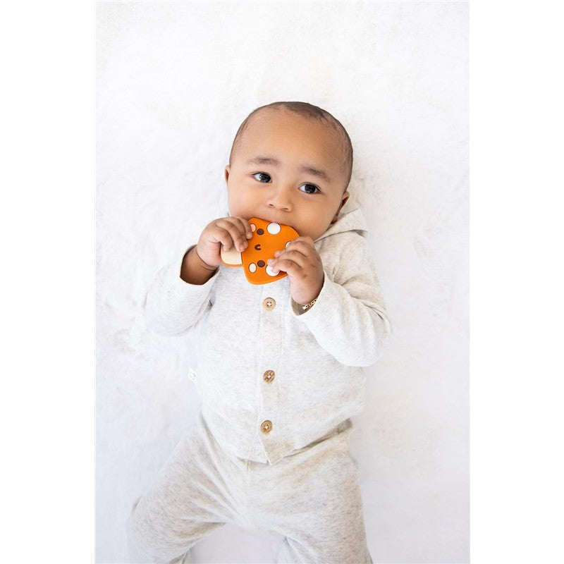 Infant holding an orange silicone mushroom teether, wearing a light gray outfit with a hood, against a soft white background.