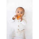 Infant holding an orange silicone mushroom teether, wearing a light gray outfit with a hood, against a soft white background.