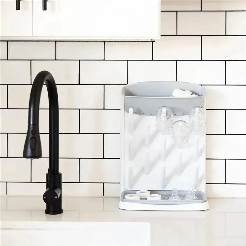 Ubbi Vertical Baby Bottle Drying Rack in gray, featuring multiple slots for drying bottles and accessories, placed on a countertop.