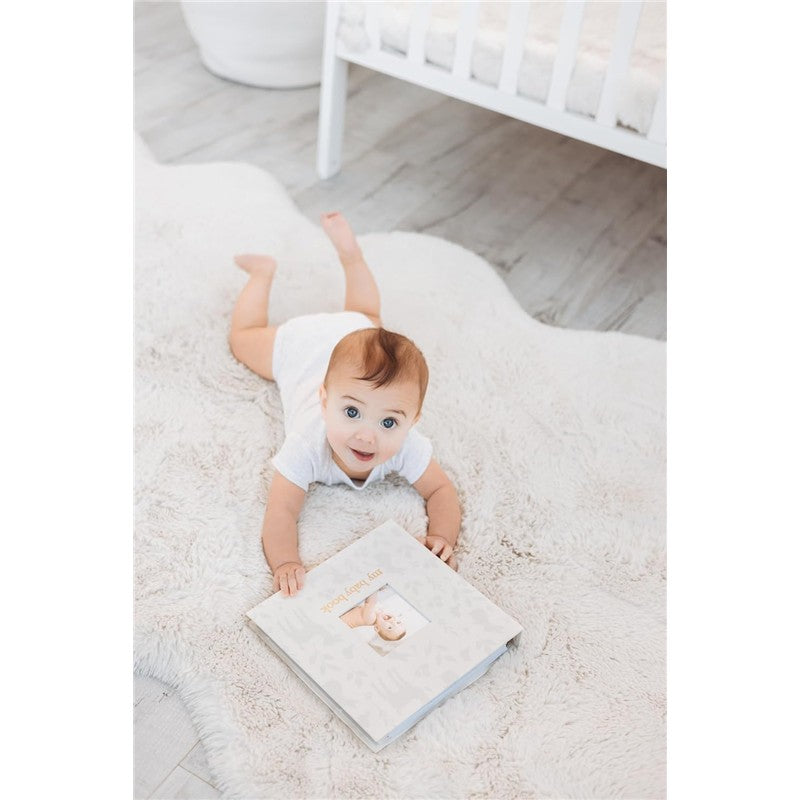 Baby crawling on a plush rug, reaching for a Pearhead Deer Print Square Baby Book featuring a window for a photo.
