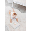 Baby crawling on a plush rug, reaching for a Pearhead Deer Print Square Baby Book featuring a window for a photo.