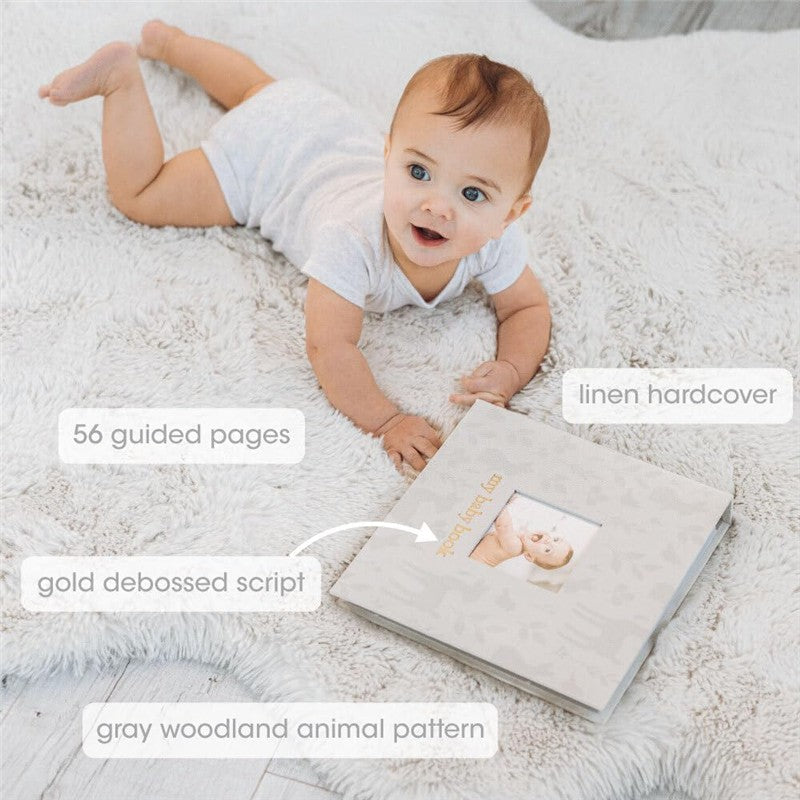 A baby lays on a fuzzy rug next to the Pearhead Deer Print Square Baby Book, featuring a linen hardcover, 56 guided pages, and a gold debossed script.
