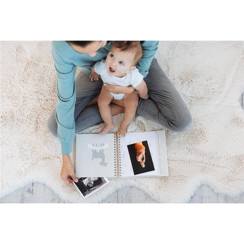 Mom and baby sitting on a soft surface, reviewing the Pearhead Deer Print Square Baby Book, filled with photos.
