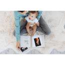 Mom and baby sitting on a soft surface, reviewing the Pearhead Deer Print Square Baby Book, filled with photos.