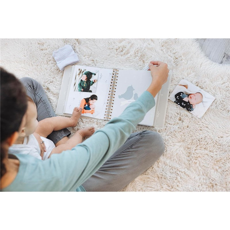 A parent holds a Pearhead Deer Print Square Baby Book open to a page with photos, sitting on a plush rug with a baby.