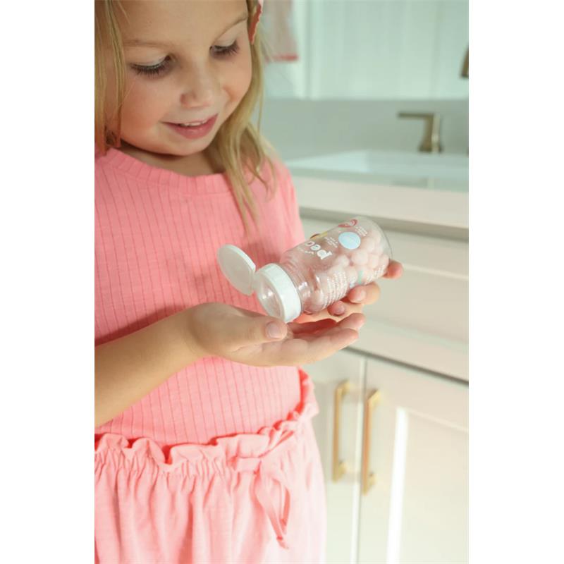 A young girl in a pink shirt holds a clear bottle of Pearl Pop bubblegum toothpaste pearls, smiling as she examines it.