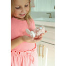 A young girl in a pink shirt holds a clear bottle of Pearl Pop bubblegum toothpaste pearls, smiling as she examines it.