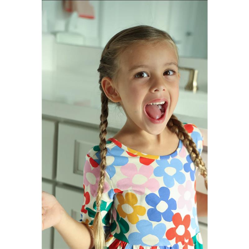 Young girl with braided hair, wearing a colorful floral dress, smiling and showing her teeth.