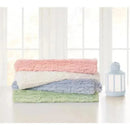 Textured faux fur stroller blankets in pink, white, blue, and green, stacked neatly on a table beside a lantern.