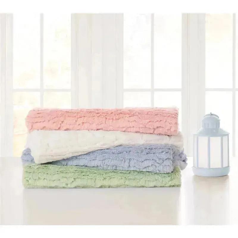 Textured faux fur stroller blankets in pink, white, blue, and green stacked on a table near a lantern.
