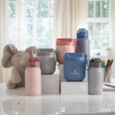 Primo Passi 12 oz insulated straw water bottles in various colors displayed on a table, next to a plush elephant toy.