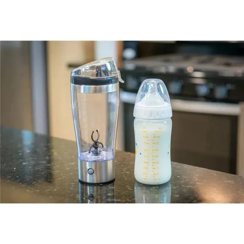 Portable Primo Passi formula mixer cup beside a baby bottle on a countertop, featuring stainless steel base and clear acrylic body.
