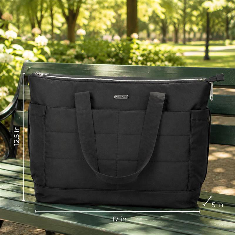 Black Primo Passi diaper bag measuring 17x12.5x5 inches, displayed on a park bench with greenery in the background.
