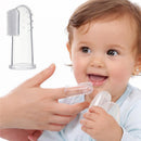Silicone finger toothbrush held by an adult finger while a smiling baby watches, with a transparent case at the bottom.