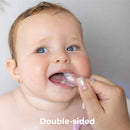 Baby uses a double-sided silicone toothbrush while a caregiver holds it; both are smiling.