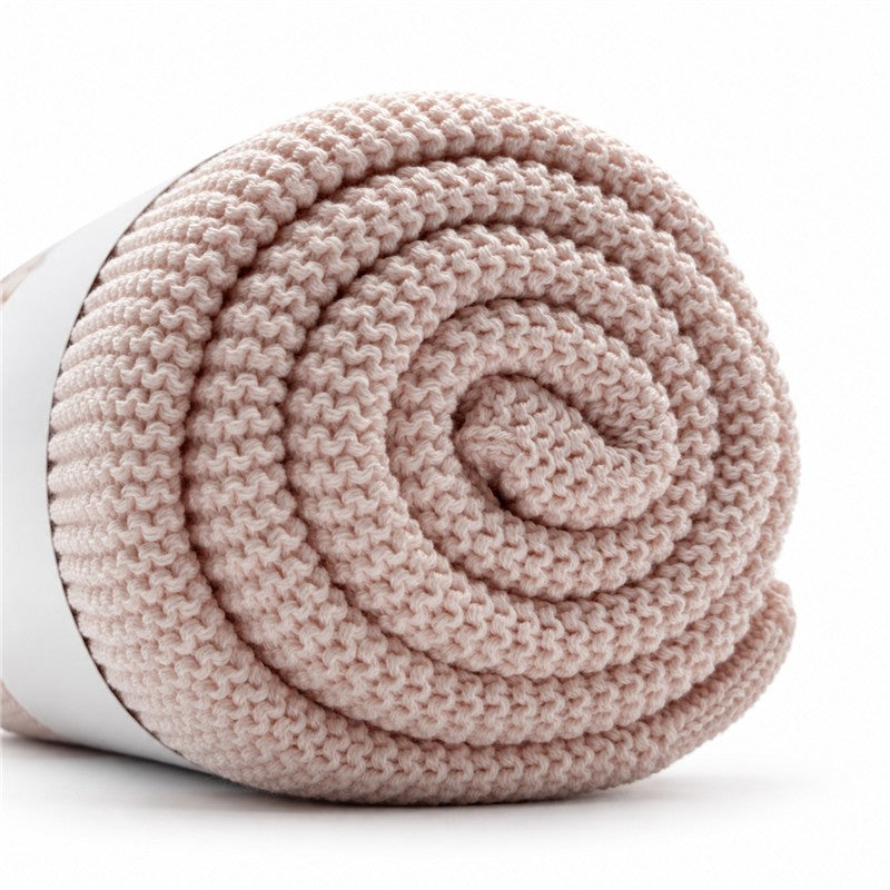 Light pink Primo Passi knit blanket rolled neatly, showcasing its soft texture and cozy design.
