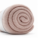 Light pink Primo Passi knit blanket rolled neatly, showcasing its soft texture and cozy design.