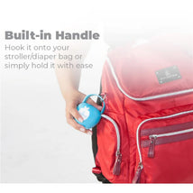 Blue Primo Passi pacifier case being held near a red diaper bag, highlighting its built-in handle feature.