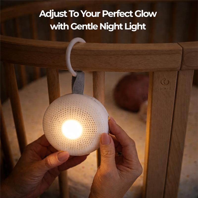 Portable baby white noise machine with a gentle night light, held near a crib, showcasing adjustable lighting features.