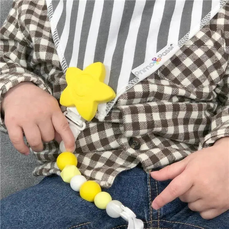 Silicone baby pacifier holder clip in the shape of a yellow star, worn by a child, with colorful beads attached.