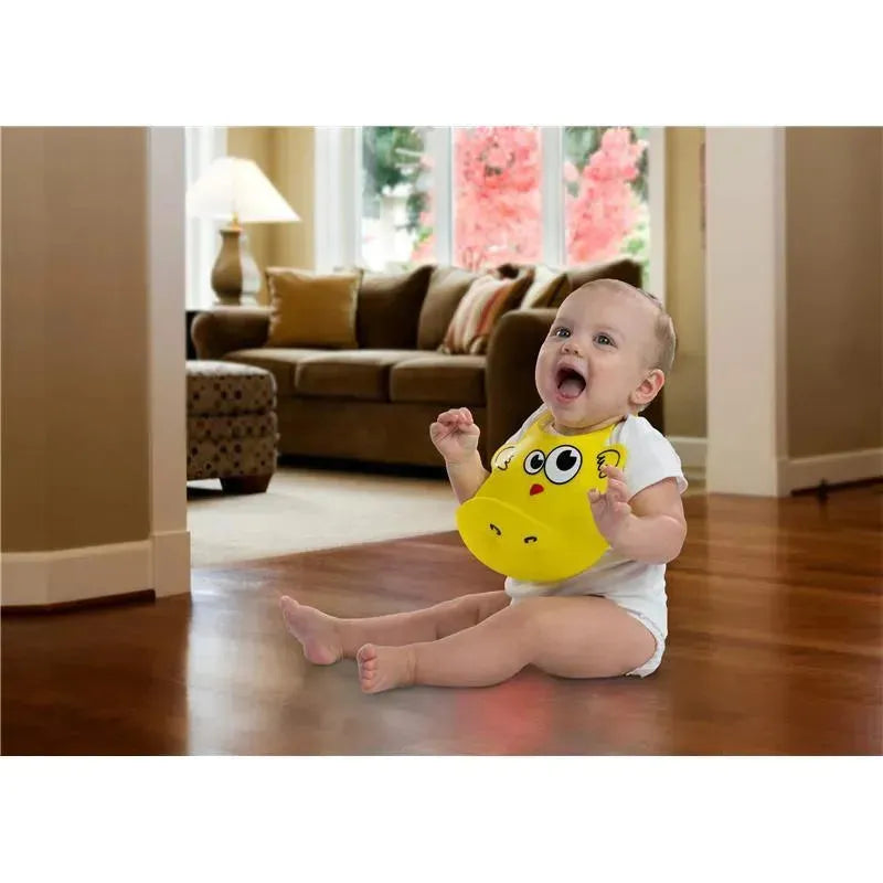Silicone baby bib in yellow with a cartoon face on a happy baby sitting on a wooden floor in a bright living room.