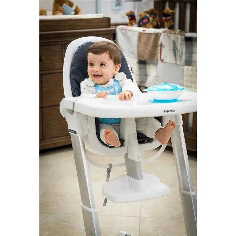 A smiling baby in a high chair, wearing a blue silicone bib, with a blue bowl on the tray.