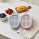 Silicone carrot-shaped ice pop molds in dusty blue and pink, placed alongside strawberries, blueberries, and mango on a marble surface.
