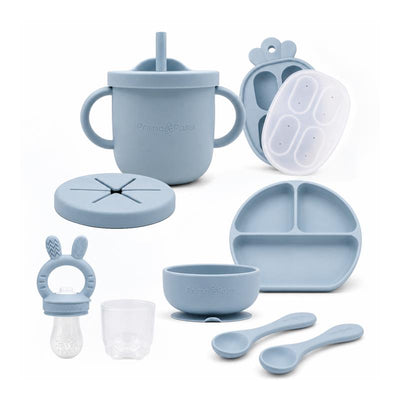 Silicone feeding set in dusty blue, including a training cup, food feeder, suction bowl, plate, and spoons.