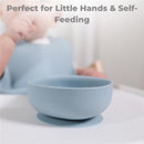 Dusty blue silicone suction bowl from Primo Passi, designed for self-feeding, with a child in the background.