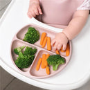A child’s hand reaches for carrots on a pink suction plate filled with broccoli and carrots.