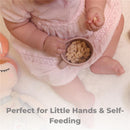 Silicone training cup in dusty blue held by a child, filled with snacks, promoting self-feeding.